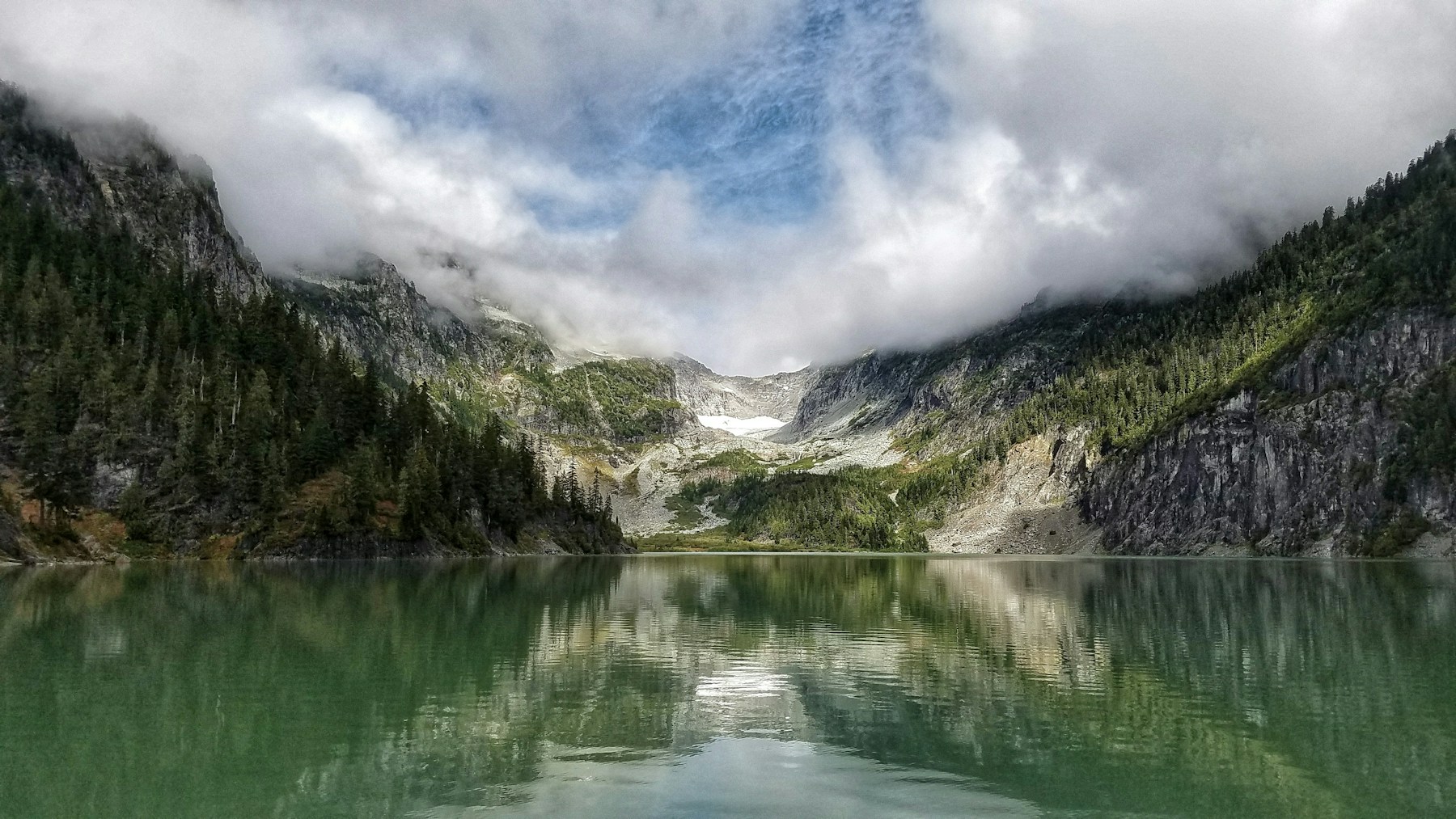 Lac montan înconjurat de pădure și nori.
